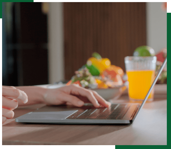 Hands typing on laptop near juice glass.